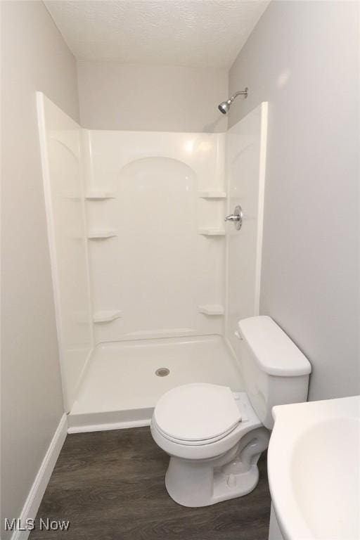 bathroom featuring toilet, baseboards, a stall shower, and wood finished floors
