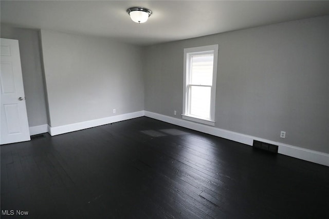 spare room with dark wood-style flooring, visible vents, and baseboards