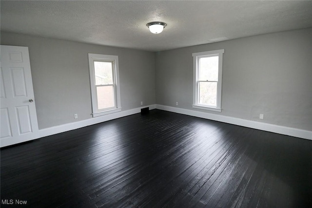 spare room with baseboards, a textured ceiling, plenty of natural light, and dark wood finished floors