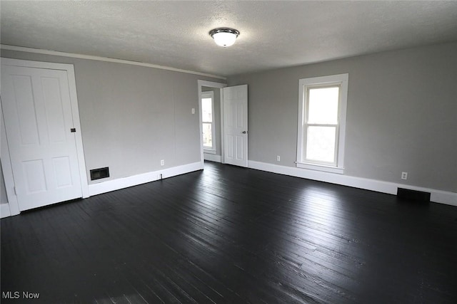 empty room featuring dark wood-type flooring, a wealth of natural light, baseboards, and a textured ceiling