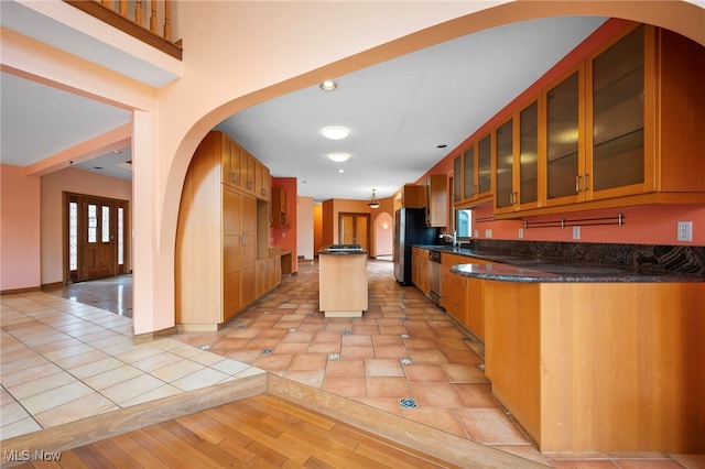 kitchen with light tile patterned floors, glass insert cabinets, arched walkways, a sink, and stainless steel appliances