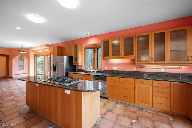 kitchen with dark stone countertops, glass insert cabinets, a sink, stainless steel appliances, and a kitchen island