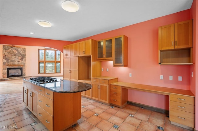 kitchen with glass insert cabinets, stainless steel gas stovetop, dark stone counters, built in study area, and a kitchen island