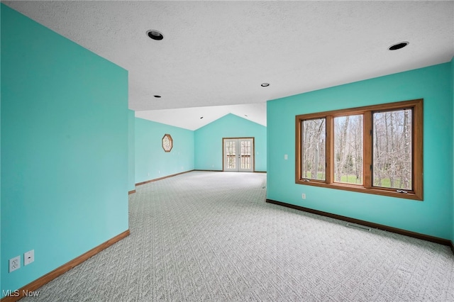empty room with carpet, a textured ceiling, visible vents, vaulted ceiling, and baseboards