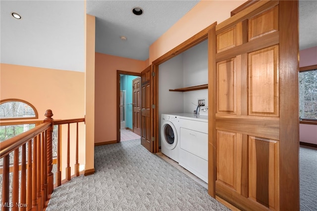 clothes washing area featuring baseboards, laundry area, a textured ceiling, washer and clothes dryer, and light colored carpet