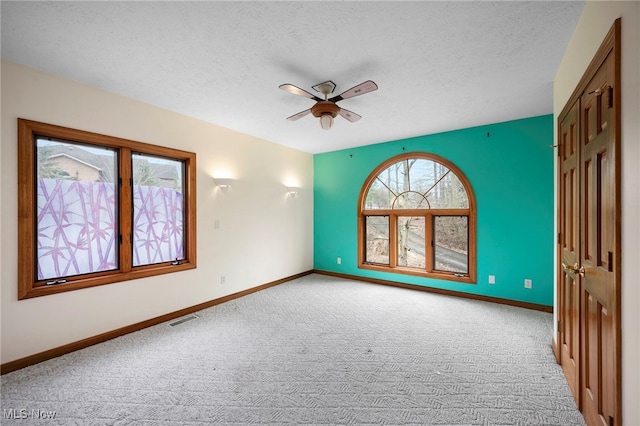 empty room featuring baseboards, carpet flooring, a textured ceiling, a ceiling fan, and visible vents