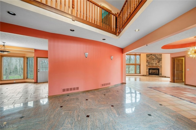 unfurnished living room featuring a high ceiling, baseboards, a stone fireplace, and visible vents
