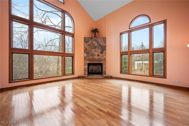unfurnished living room featuring light wood-style floors, high vaulted ceiling, baseboards, and plenty of natural light