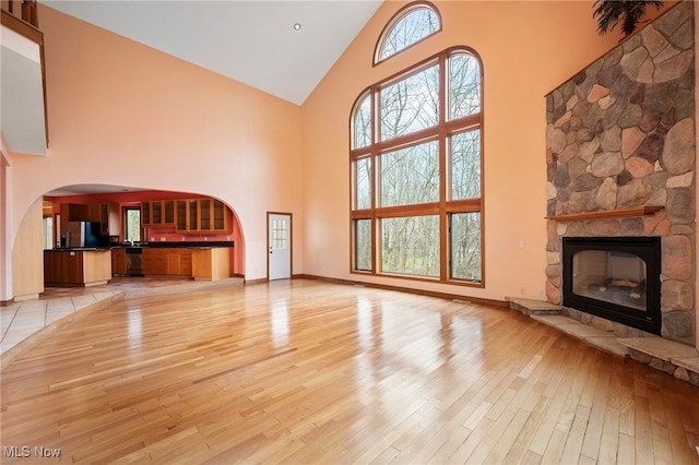 unfurnished living room featuring light wood-style floors, high vaulted ceiling, baseboards, and a stone fireplace
