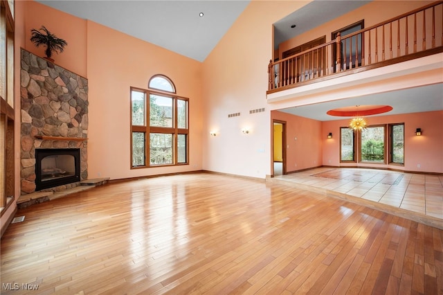 unfurnished living room featuring a fireplace, visible vents, a high ceiling, baseboards, and hardwood / wood-style flooring
