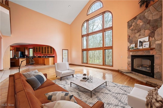 living area featuring high vaulted ceiling, arched walkways, light wood finished floors, and a fireplace