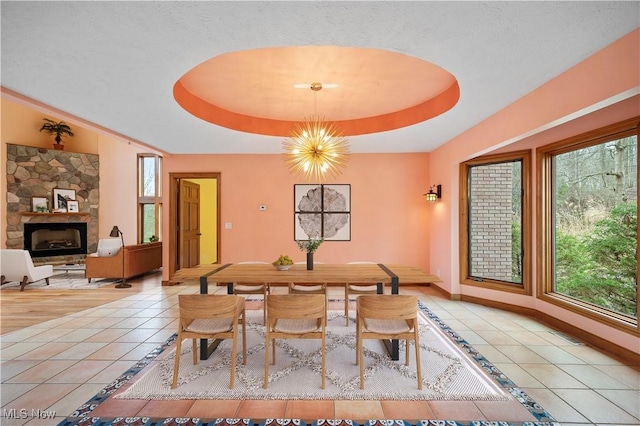 dining room with a stone fireplace, a raised ceiling, light tile patterned flooring, and baseboards
