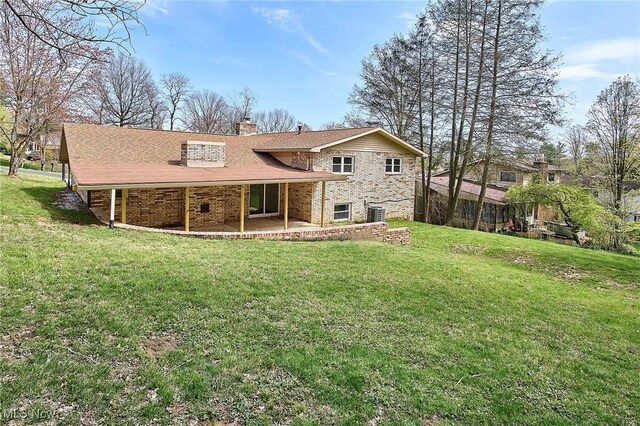 back of house with a lawn, a chimney, a shingled roof, a patio, and brick siding