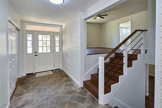 entryway featuring stone finish flooring, baseboards, brick wall, and stairs