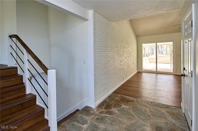 interior space featuring brick wall, wood finished floors, baseboards, and stairway
