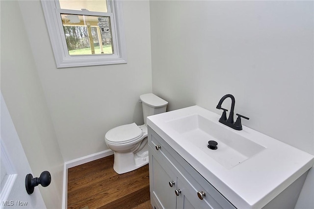 half bath with baseboards, wood finished floors, vanity, and toilet