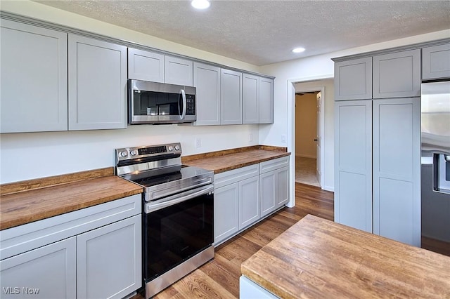 kitchen featuring a textured ceiling, recessed lighting, wood finished floors, butcher block counters, and appliances with stainless steel finishes