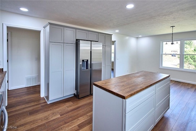 kitchen featuring a textured ceiling, wood counters, stainless steel fridge, dark wood finished floors, and visible vents