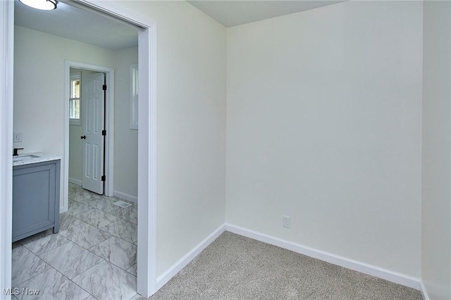 hallway featuring marble finish floor, baseboards, and a sink