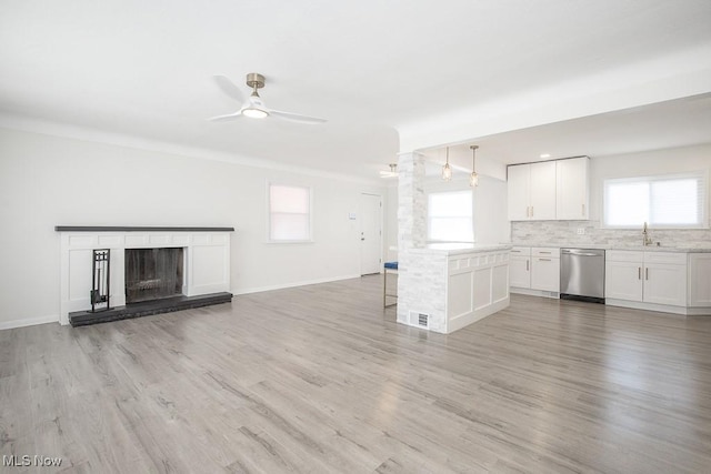 unfurnished living room featuring ceiling fan, light wood-type flooring, a fireplace with raised hearth, a sink, and baseboards