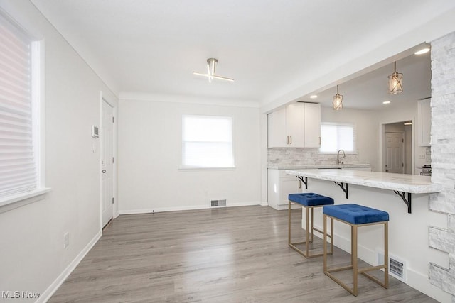 kitchen featuring a kitchen bar, white cabinetry, visible vents, light wood finished floors, and backsplash