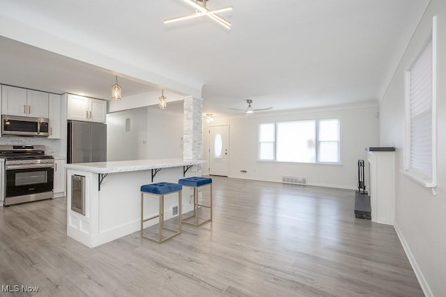 kitchen featuring open floor plan, light countertops, stainless steel appliances, light wood-style flooring, and a breakfast bar area