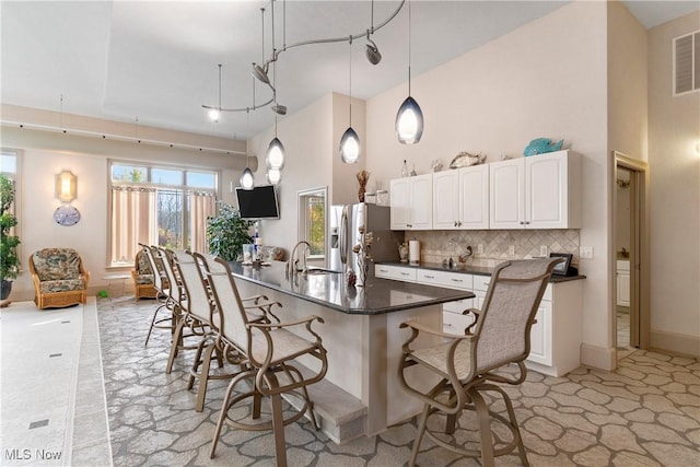 2142 State St NW, Uniontown, OH 44685 - kitchen featuring stainless steel refrigerator with ice dispenser, dark countertops, a kitchen breakfast bar, a towering ceiling, and backsplash