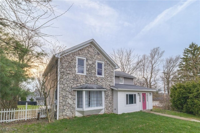 view of home's exterior with fence, stone siding, and a lawn