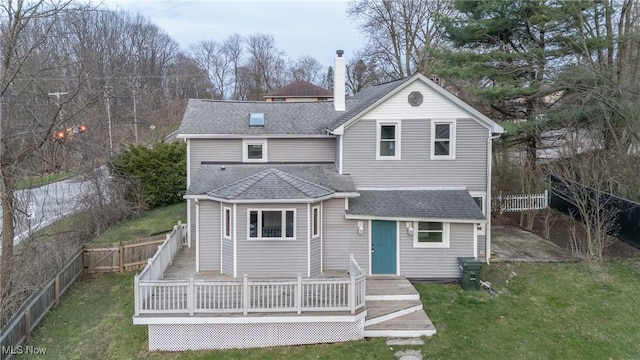 back of property with a fenced backyard, a shingled roof, a wooden deck, and a lawn