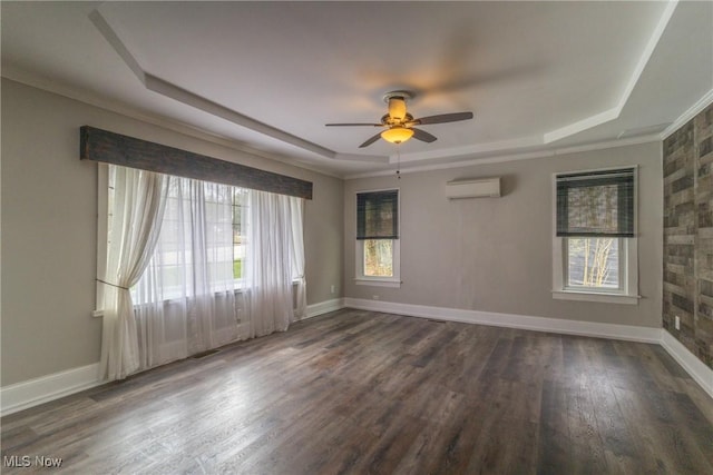 empty room with a wall mounted air conditioner, a tray ceiling, baseboards, and wood finished floors