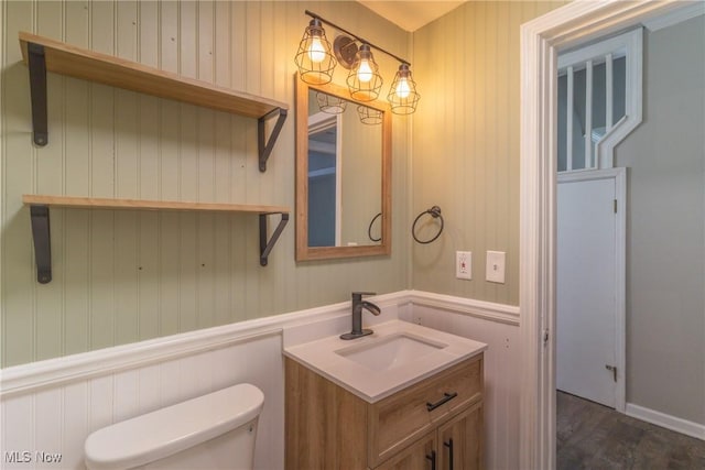 half bath featuring toilet, vanity, and wainscoting