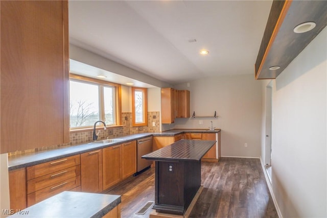 kitchen featuring dark wood-type flooring, dishwasher, a sink, and backsplash