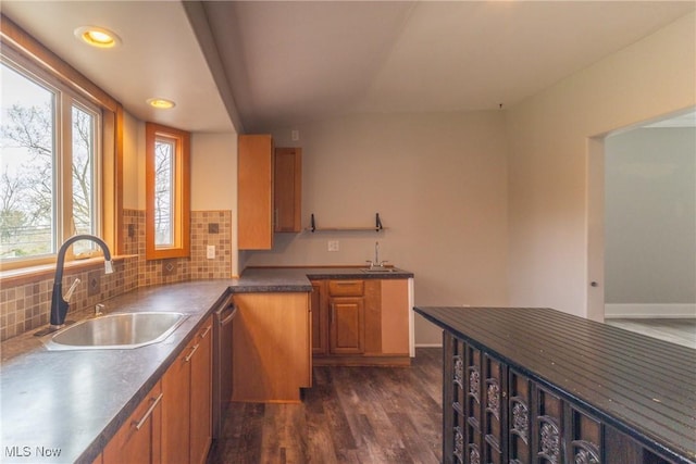 kitchen featuring tasteful backsplash, dark wood-style floors, dark countertops, brown cabinets, and a sink