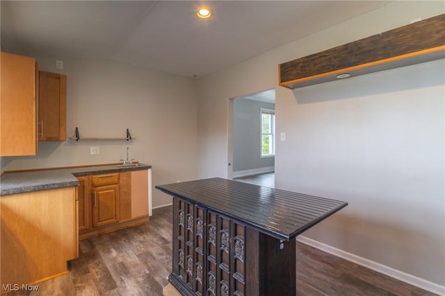 kitchen featuring baseboards, recessed lighting, dark countertops, dark wood finished floors, and a sink