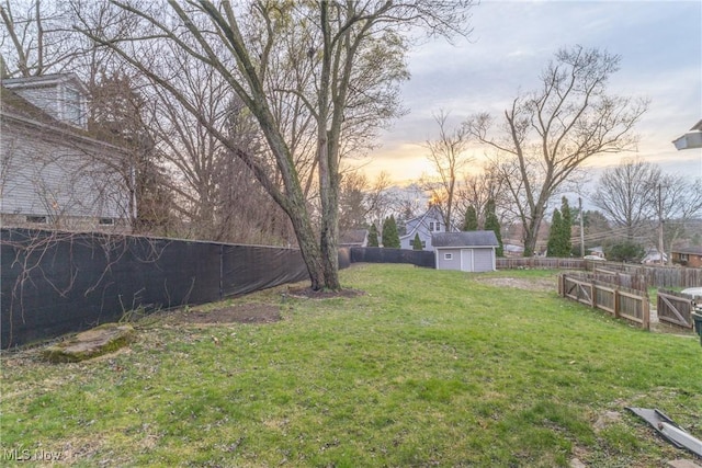 yard at dusk featuring a shed, a fenced backyard, an outdoor structure, and a garage