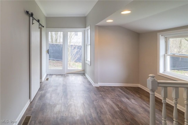 spare room featuring a barn door, dark wood-style flooring, baseboards, and a healthy amount of sunlight
