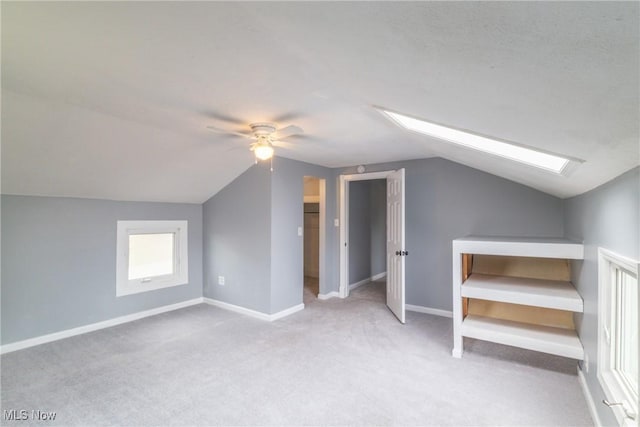additional living space with vaulted ceiling with skylight, baseboards, a ceiling fan, and carpet flooring