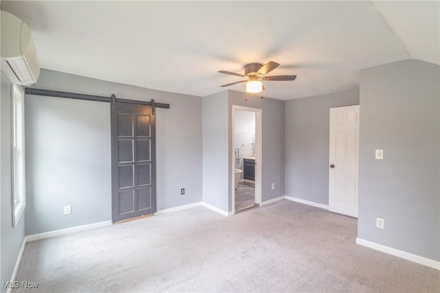 unfurnished bedroom featuring an AC wall unit, baseboards, a barn door, ceiling fan, and carpet
