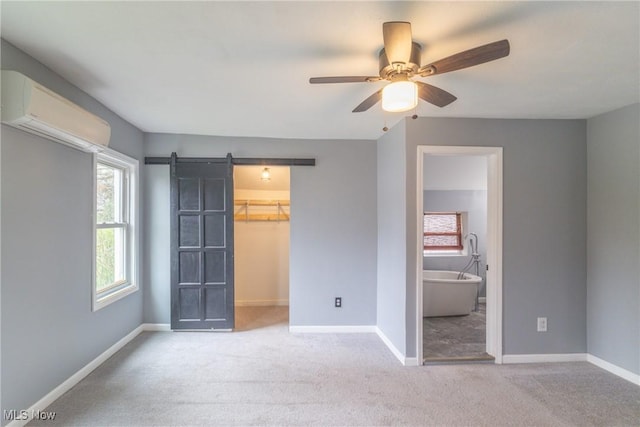 unfurnished bedroom with carpet, a spacious closet, a barn door, an AC wall unit, and baseboards
