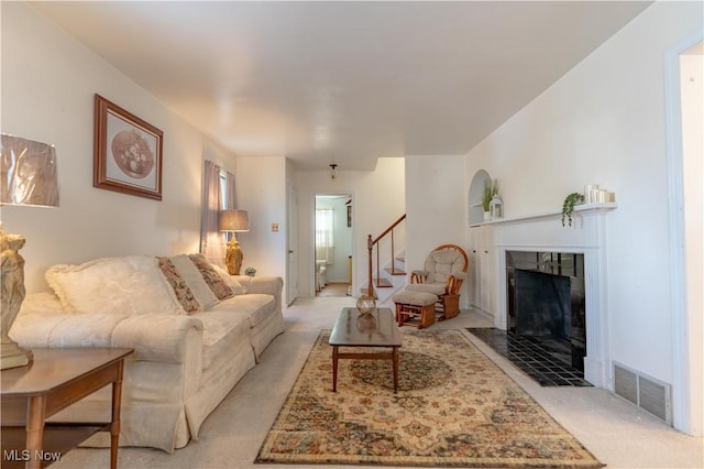 living area featuring visible vents, a tiled fireplace, light carpet, and stairway