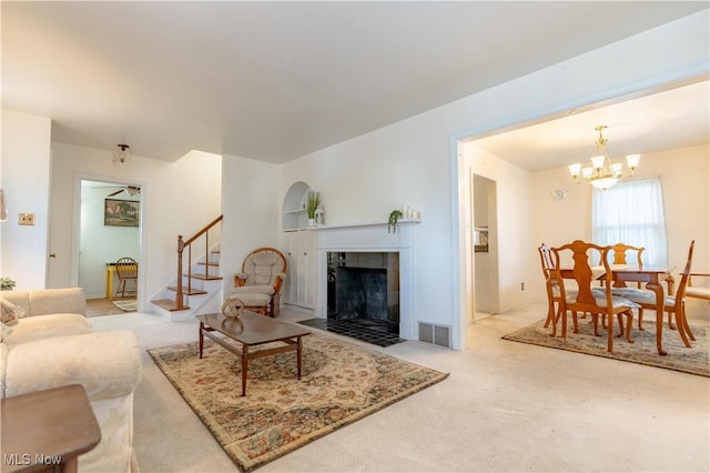 carpeted living room featuring a tiled fireplace, visible vents, stairs, and a notable chandelier