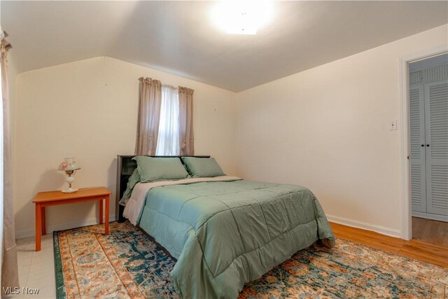 bedroom with baseboards, light wood-style flooring, and lofted ceiling