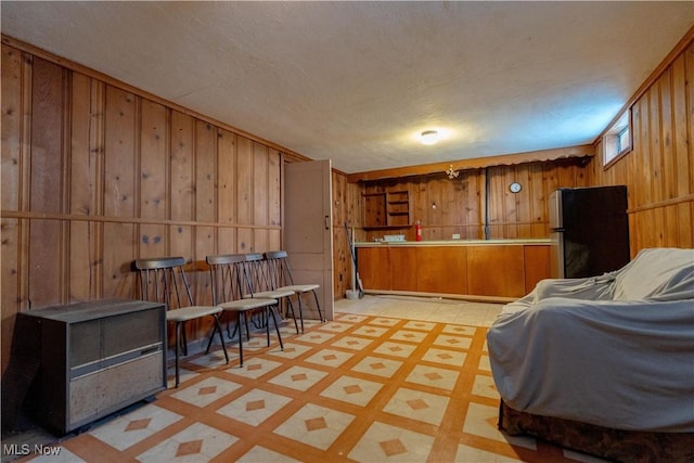 bar featuring wooden walls, freestanding refrigerator, and light floors