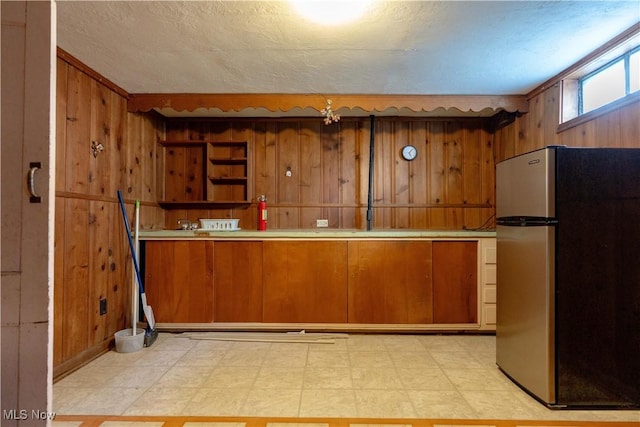 kitchen with brown cabinets, light countertops, wood walls, freestanding refrigerator, and light floors