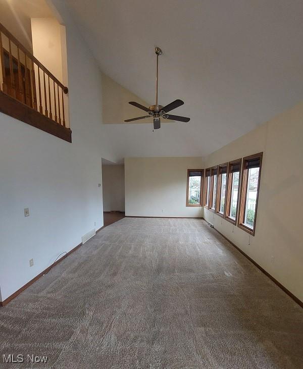 carpeted spare room featuring high vaulted ceiling, visible vents, baseboards, and a ceiling fan