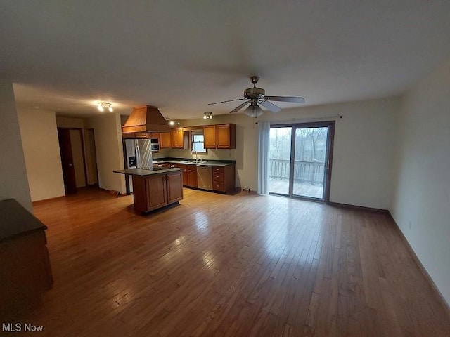 kitchen featuring a sink, appliances with stainless steel finishes, dark countertops, light wood finished floors, and a kitchen island
