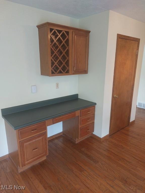 unfurnished office featuring baseboards, built in study area, dark wood-style floors, a bar, and visible vents
