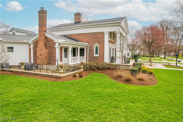 128 Center St, Milan, OH 44846 - back of property featuring a chimney, a yard, covered porch, brick siding, and central AC