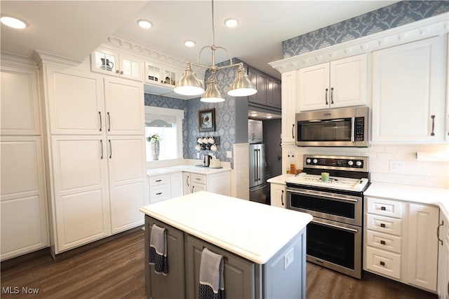 128 Center St, Milan, OH 44846 - kitchen with white cabinets, appliances with stainless steel finishes, light countertops, wallpapered walls, and dark wood-type flooring