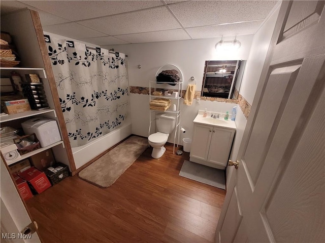 bathroom featuring toilet, a paneled ceiling, shower / bathtub combination with curtain, vanity, and wood finished floors